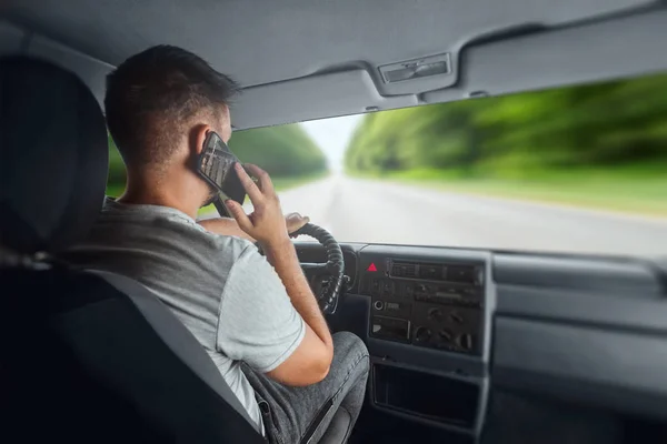Muž za volantem, držící v ruce smartphone, porušuje dopravní předpisy. Koncept nehody, narušení provozu, telefon za volantem — Stock fotografie