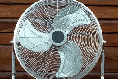 Ahşap bir duvarın arka planına karşı masa üzerinde büyük masa üstü vantilatör. Isı kavramı, sıcak hava, klima