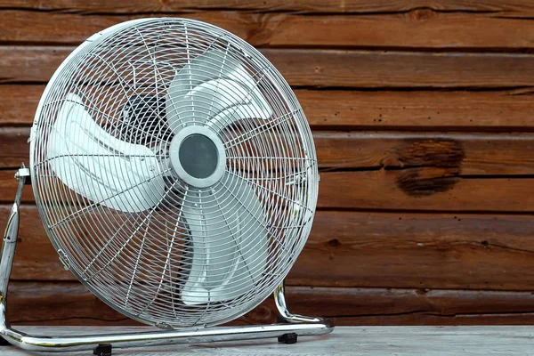 Ventilador de mesa grande sobre la mesa sobre el fondo de una pared de madera. El concepto de calor, clima caliente, aire acondicionado — Foto de Stock