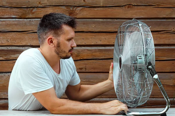 Uomo sudato di fronte a un ventilatore di raffreddamento, rinfrescante nel concetto di estate calda. Il concetto di salvezza dal caldo, dal caldo, da un condizionatore primitivo — Foto Stock