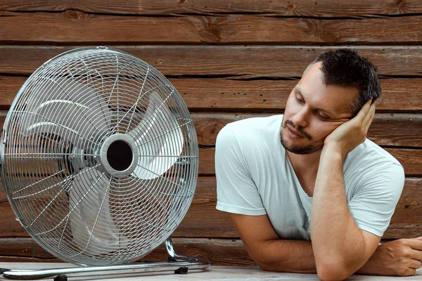 Sweaty man in front of a cooling ventilator, refreshing in the concept of hot summer. The concept of salvation from the heat, hot weather, a primitive air conditioner — Stock Photo, Image