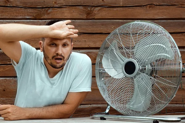 Uomo sudato di fronte a un ventilatore di raffreddamento, rinfrescante nel concetto di estate calda. Il concetto di salvezza dal caldo, dal caldo, da un condizionatore primitivo — Foto Stock