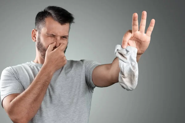 En ung man håller sina illaluktande strumpor och täcker näsan med handen. Obehaglig lukt. Stinkande ben, svamp på benen — Stockfoto