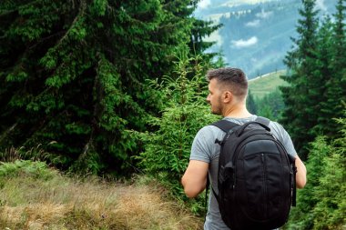 Bir sırt çantası ile erkek turist manzara hayran bir dağın tepesinde duruyor. Aktif tatil kavramı, seyahat, dağlarda tatil, yaşam tarzı