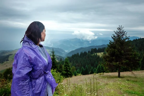 Porträt eines schönen Mädchens in Regenmantel und weißer Mütze vor dem Hintergrund der wunderschönen Karpatenberge. Reisekonzept, Freizeitgestaltung, Urlaub — Stockfoto