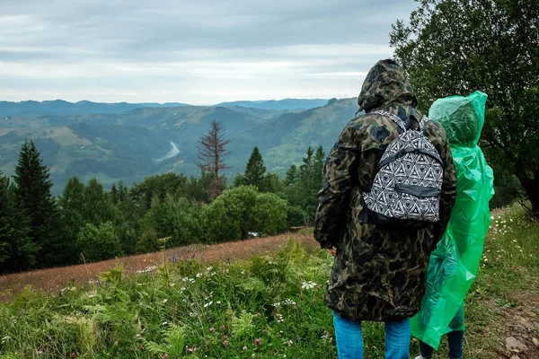 Pareja, turistas en un impermeable sobre un fondo de hermosas montañas Cárpatos. Levántate en las montañas. Concepto de viaje, actividad de ocio, vacaciones —  Fotos de Stock