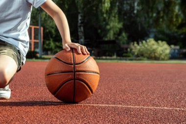 Çocuk elinde bir basketbol yakın çekim tutar, bir basketbol sahası arka plan karşı. Bir spor yaşam tarzı kavramı, eğitim, spor, eğlence, tatil.