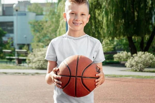 Retrato de um rapaz com um basquetebol num campo de basquetebol. O conceito de um estilo de vida esportivo, treinamento, esporte, lazer, férias . — Fotografia de Stock