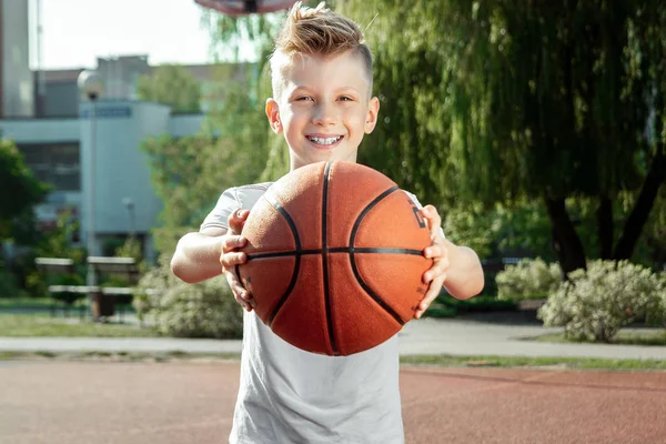 Retrato de um rapaz com um basquetebol num campo de basquetebol. O conceito de um estilo de vida esportivo, treinamento, esporte, lazer, férias . — Fotografia de Stock