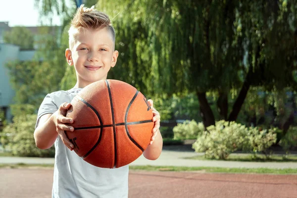 Retrato de um rapaz com um basquetebol num campo de basquetebol. O conceito de um estilo de vida esportivo, treinamento, esporte, lazer, férias . — Fotografia de Stock