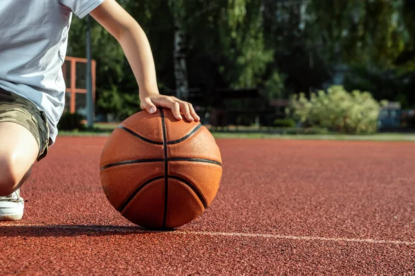 O menino segura em suas mãos um close up de basquete, contra o pano de fundo de um campo de basquete. O conceito de um estilo de vida esportivo, treinamento, esporte, lazer, férias . — Fotografia de Stock