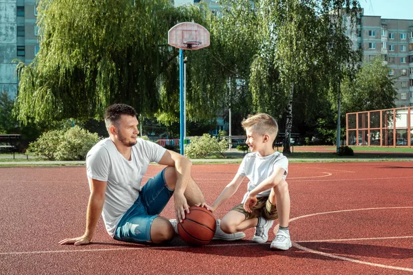 Father and son play basketball together at the basketball court. father spends time with the child, sporty lifestyle, training, rest, vacation.