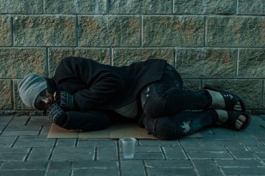 Bir adam, evsiz, yardım işaretiyle sokakta soğuk zeminde uyuyan bir adam. Evsiz bir kişi kavramı, sosyal sorun, bağımlı, yoksulluk, umutsuzluk.