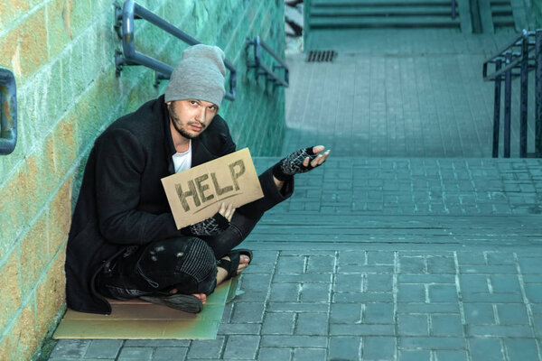 A man, homeless, a person asks for alms on the street with a Help sign. Concept of homeless person, addict, poverty, despair.