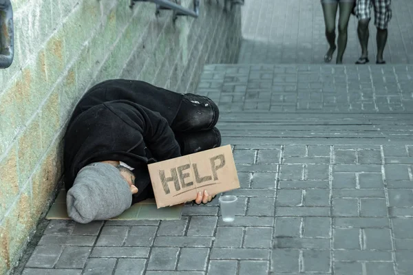 A man, homeless, a person asks for alms on the street with a Help sign. Concept of homeless person, addict, poverty, despair.
