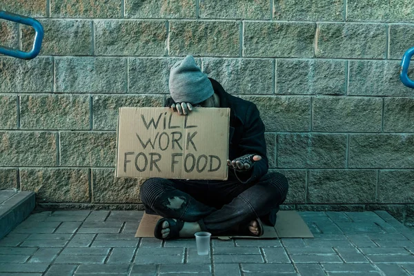 En man, hemlösa, en man ber om allmosor på gatan med ett tecken kommer att arbeta för mat. Begreppet hemlösa person, missbrukare, fattigdom, förtvivlan. — Stockfoto