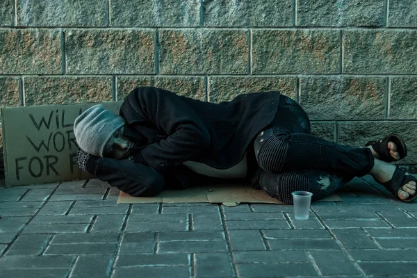 En man, hemlösa, en man sover på ett kallt golv på gatan med ett hjälp tecken. Begreppet hemlösa person, sociala problem, missbrukare, fattigdom, förtvivlan. — Stockfoto