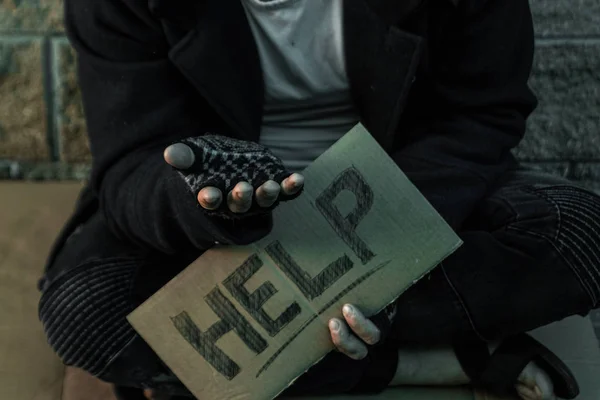 A man, homeless, a person asks for alms on the street with a Help sign. Concept of homeless person, addict, poverty, despair.