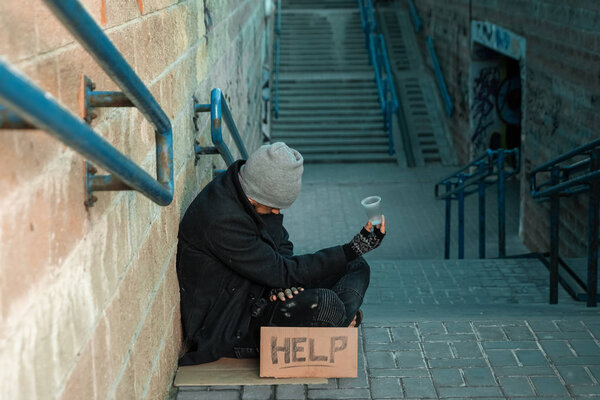 Мужчина, бездомный, мужчина, спящий на холодном полу на улице с табличкой "Помощь". Бездомный, социальная проблема, добавка, бедность, воздух
.