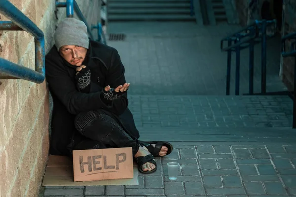 Un uomo, senzatetto, un uomo che dorme su un pavimento freddo per strada con un cartello d'aiuto. Concetto di senzatetto, problema sociale, tossicodipendente, povertà, disperazione . — Foto Stock