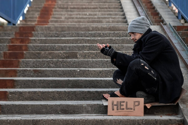Человек, бездомный, человек просит милостыню на улице с табличкой "Помощь". Концепция бездомного, наркоман, бедность, отчаяние
.