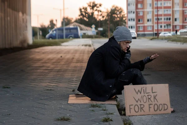 En man, hemlösa, en man ber om allmosor på gatan med ett tecken kommer att arbeta för mat. Begreppet hemlösa person, sociala problem, missbrukare, fattigdom, förtvivlan. — Stockfoto