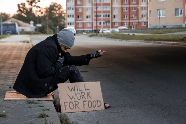 Un uomo, senzatetto, un uomo chiede elemosina per strada con un cartello funzionerà per il cibo. Concetto di senzatetto, problema sociale, tossicodipendente, povertà, disperazione . — Foto Stock