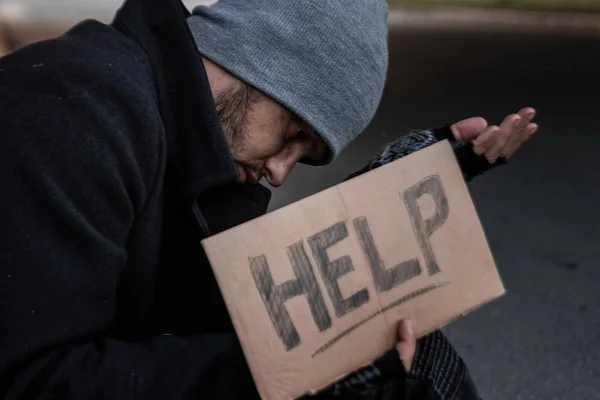 ホームレスの男が、ヘルプサインを持って路上でアルムを求める。ホームレスの概念、中毒者、貧困、絶望. — ストック写真