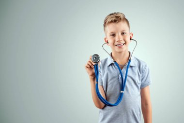 Gülümseyen çocuk, izole ışık arka plan üzerinde elinde bir stetoskop tutan. Tıp eğitimi, meslek seçimi, geleceğin doktoru.