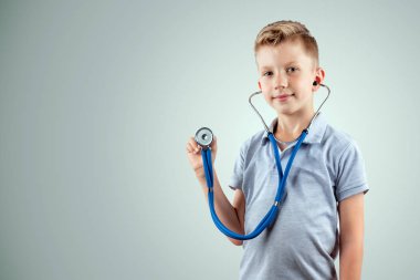 Gülümseyen çocuk, izole ışık arka plan üzerinde elinde bir stetoskop tutan. Tıp eğitimi, meslek seçimi, geleceğin doktoru.