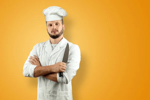 留着胡须的男人，一个戴着帽子的厨师，手里拿着一把刀，在黄色的背景上被隔离了。烹饪， 食谱， 美食. — 图库照片
