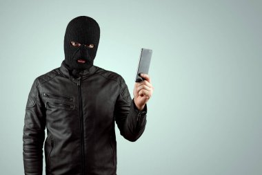 Soyguncu, elinde hafif bir arka planda bir telefonla bir balaclava'da haydut. Soygun, hacker, suç, hırsızlık. Kopyalama alanı.
