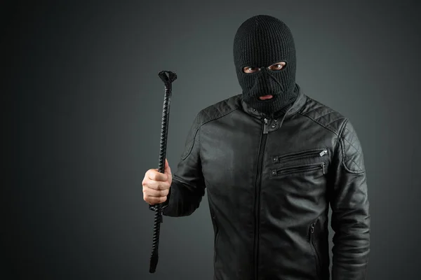 Robber, bandit in a balaclava with a crowbar in his hands on a black background. Robbery, hacker, crime, theft. Copy space.