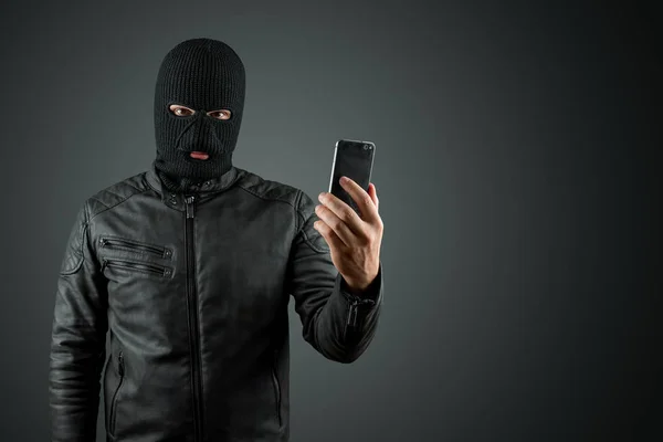 Грабіжник, бандит у балаклаві з телефоном у руках на чорному тлі. Пограбування, хакер, злочинність, крадіжка. Копіювати простір — стокове фото