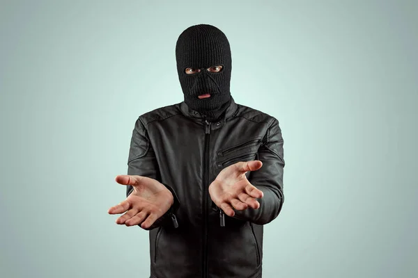 Robber, bandit in a balaclava surrenders on a light background. Robbery, hacker, crime, theft. Copy space.