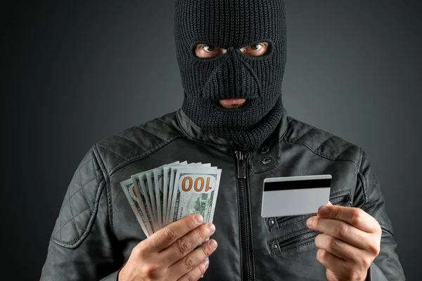 발라클라바의 깡패인 강도가 어두운 배경에 신용카드를 손에 들고 있다. 강도, 해커, 범죄, 절도. 복사 공간. — 스톡 사진