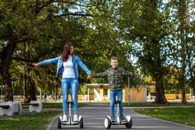 Anne ve oğlu parkta bir hoverboard binmek, kendini dengeleyen scooter. Bebek teknolojisi geleceği ile aktif yaşam tarzı süresi
