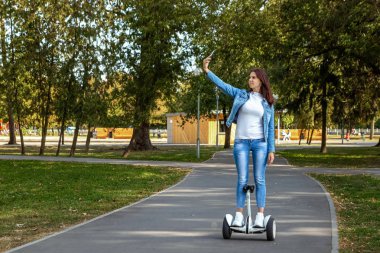Parkta uçan kaykayla uçan güzel bir kız, kendi kendini dengeleyen bir scooter. Etkin yaşam tarzı teknolojisi gelecekteki kopyalama alanı