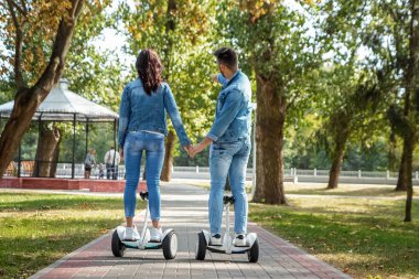 Parkta hoverboard'a binen genç bir çift, kendini dengeleyen bir scooter. Aktif yaşam tarzı teknolojisi gelecek