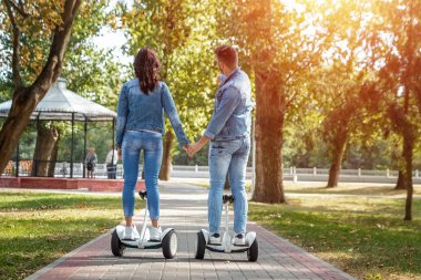 Parkta hoverboard'a binen genç bir çift, kendini dengeleyen bir scooter. Aktif yaşam tarzı teknolojisi gelecek