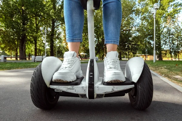 Piernas de una chica en zapatillas blancas en un hoverboard blanco, scooter autoequilibrado en un primer plano del parque. Estilo de vida activo tecnología futuro espacio de copia — Foto de Stock