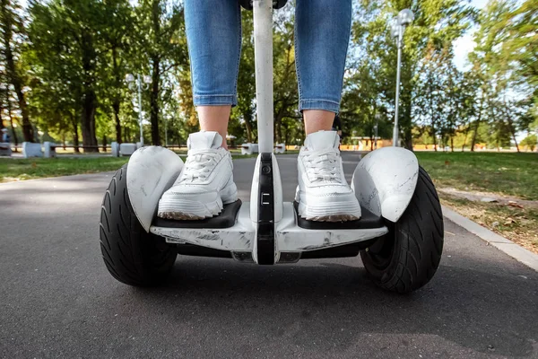 Piernas de una chica en zapatillas blancas en un hoverboard blanco, scooter autoequilibrado en un primer plano del parque. Estilo de vida activo tecnología futuro espacio de copia — Foto de Stock