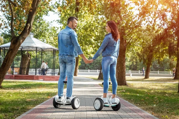 Egy fiatal házaspár lovaglás hoverboard egy parkban, önkiegyensúlyozó robogó. Az aktív életmód-technológia jövője — Stock Fotó