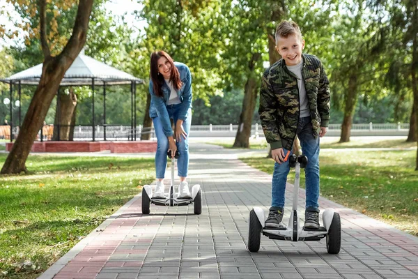 Anne ve oğlu parkta bir hoverboard binmek, kendini dengeleyen scooter. Bebek teknolojisi geleceği ile aktif yaşam tarzı süresi — Stok fotoğraf