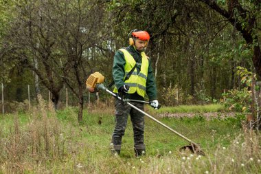Profesyonel kıyafetli bir işçi, çim biçme makinesiyle çim biçer. Çim biçme, yol kenarları, kenar