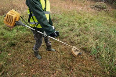 Profesyonel kıyafetli bir işçi, çim biçme makinesiyle çim biçer. Çim biçme, yol kenarları, kenar