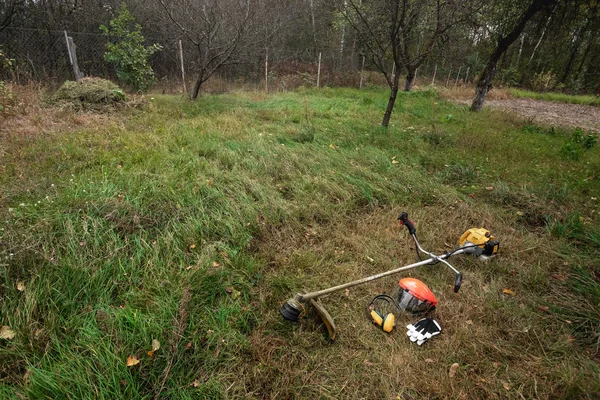 Werkzeuge und Geräte zum Rasenmähen, der Rasen liegt auf dem Boden, ein Rasentrimmer. Rasenmähen, Straßenränder mähen, Gras mähen. — Stockfoto