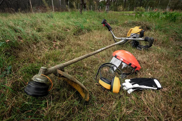 Herramientas y equipos para cortar hierba, el césped se encuentra en el suelo, una podadora de hierba. Cortar césped, bordes de la carretera, cortar hierba . —  Fotos de Stock