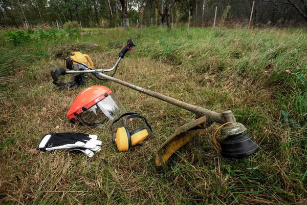 Herramientas y equipos para cortar hierba, el césped se encuentra en el suelo, una podadora de hierba. Cortar césped, bordes de la carretera, cortar hierba . —  Fotos de Stock
