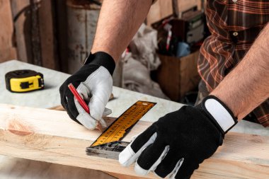 Marangoz, tahta kesim tahtasındaki işaretlerin üzerinde kurşun kalemle, erkek eli de tahta tahtaya yakın bir kalemle not alıyor. Ahşap